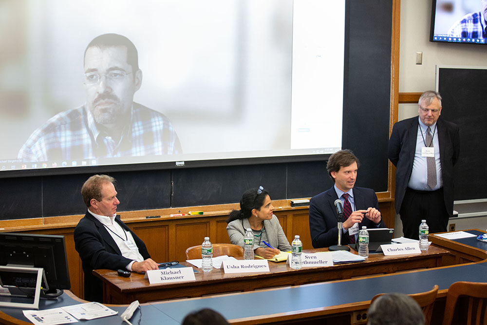 Charles W. Allen answering a question, while Stanford Law Prof. Michael Klausner &#039;81 (far left), Baylor U. Hankamer Bus. Prof. Mike Stegemoller (on screen), U. of Georgia Law Prof. Usha Rodrigues (left), and YLS Clinical Associate Prof. Sven Riethmueller (right) listen